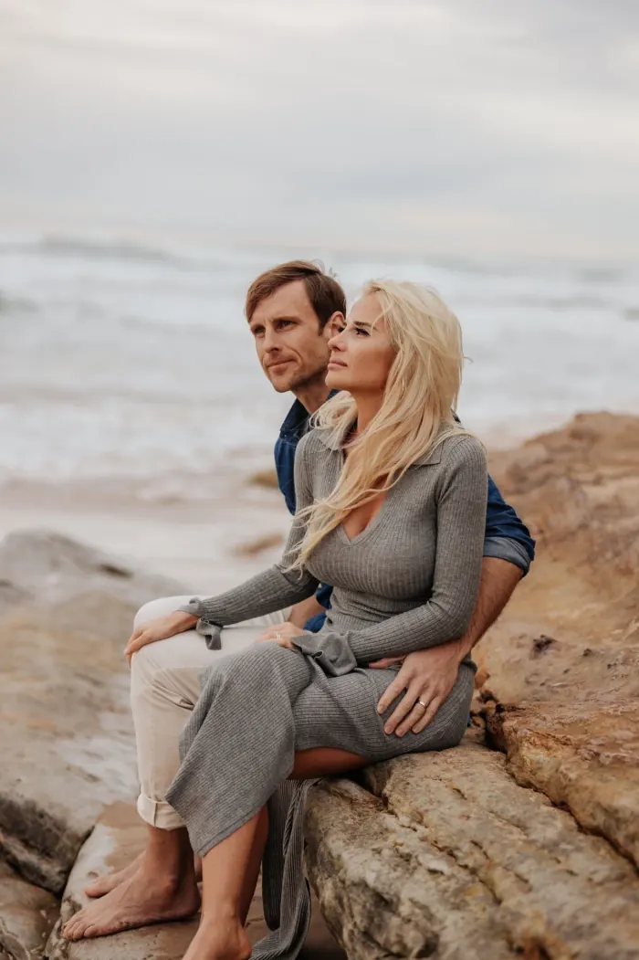 Julia and Mike sitting together on rocks by the sea.
